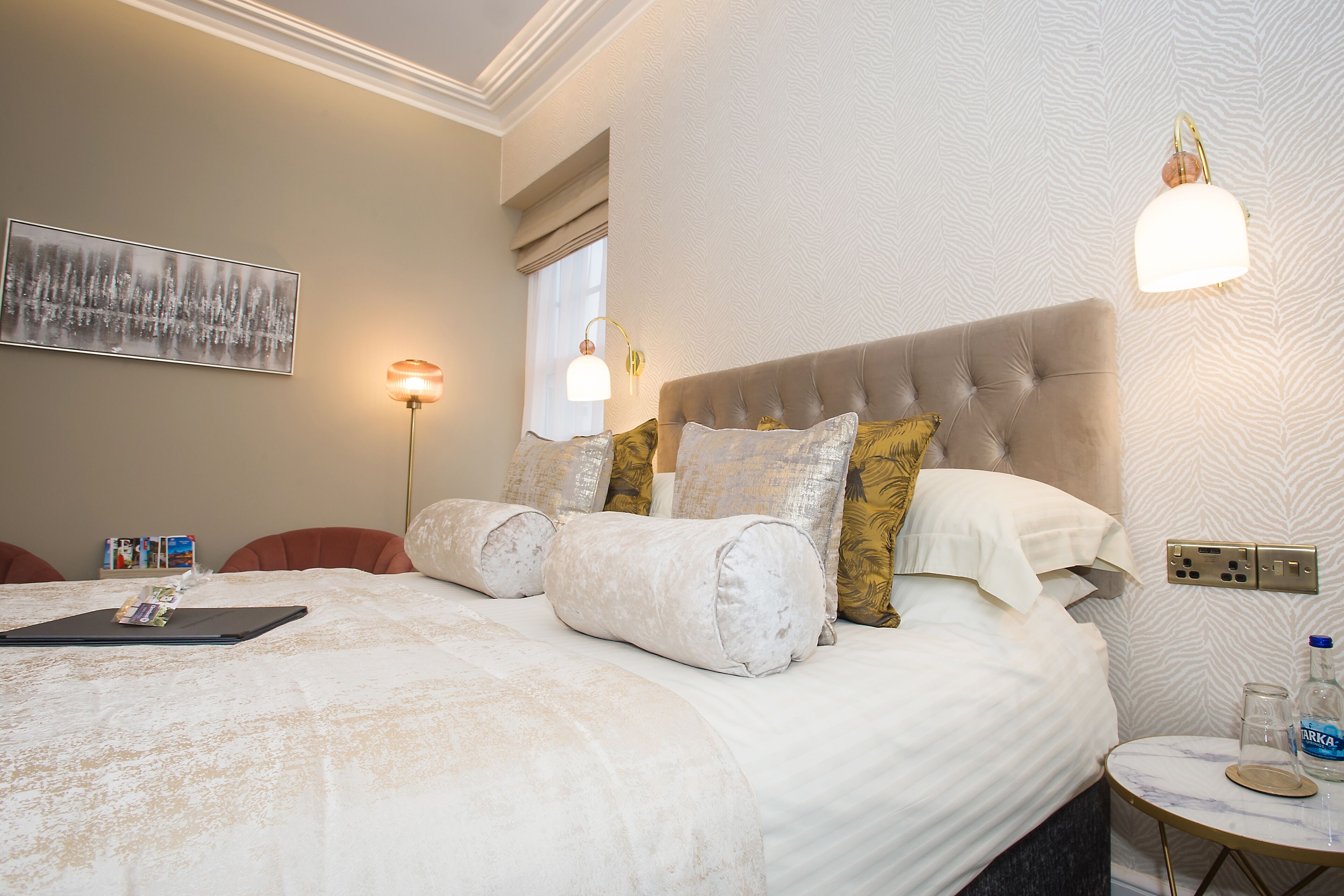 Ein ordentlich gemachtes Bett mit Kopfteil, ein Nachttisch mit Lampe und eine Wandleuchte.