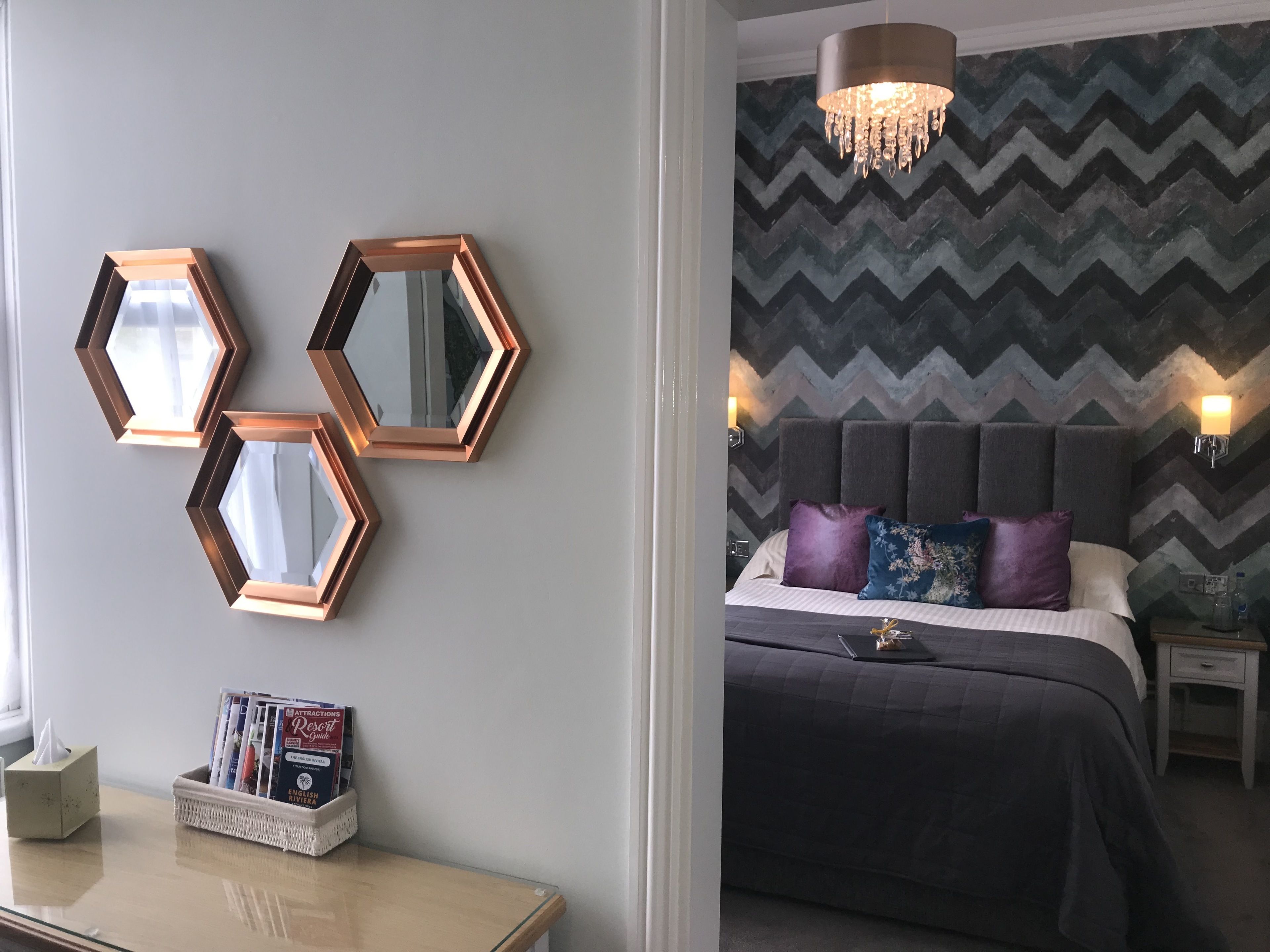 A bedroom with a bed, a nightstand, a bedside table, and a wall-mounted mirror.
