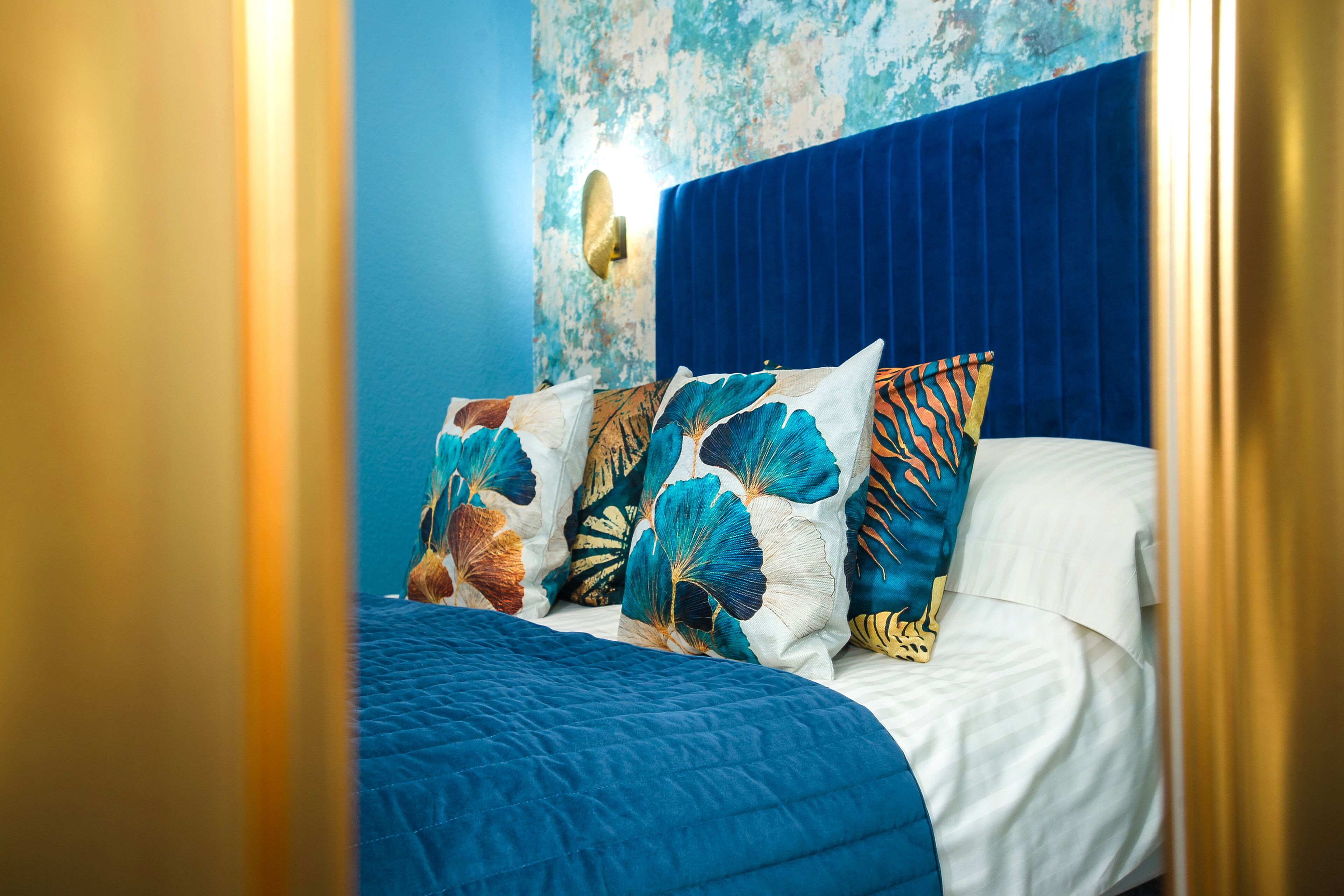 Un lit avec une tête de lit bleue et des oreillers à motifs floraux.