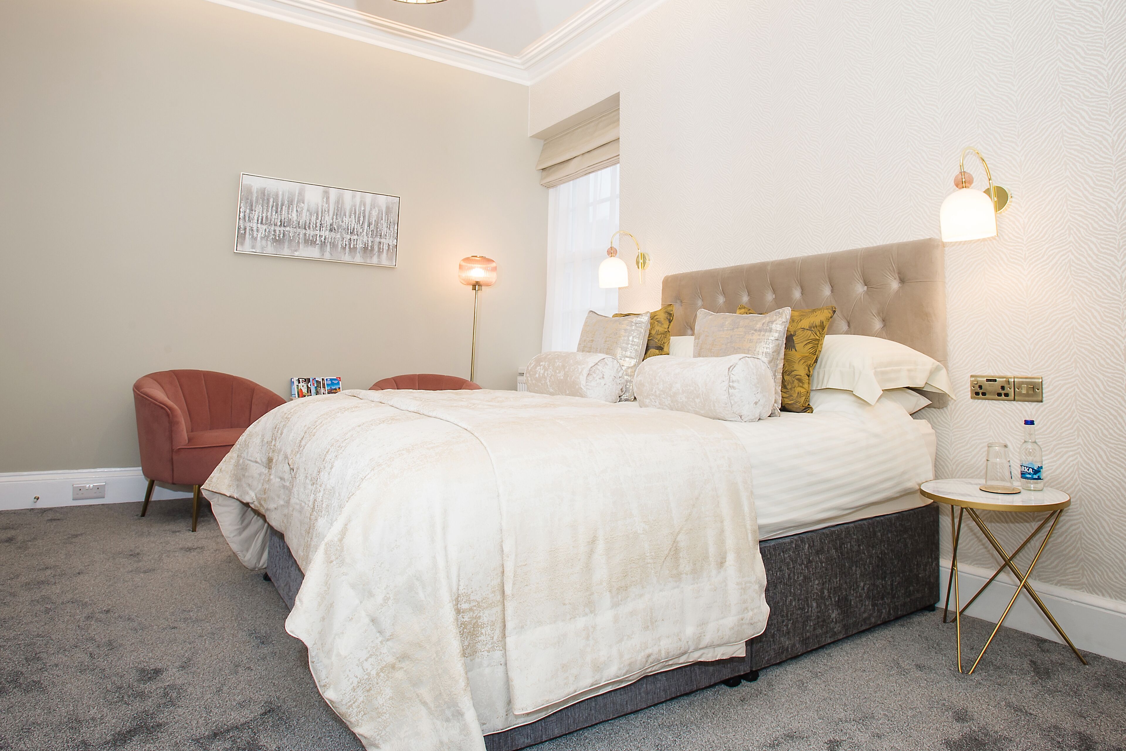 Un dormitorio con una cama grande, una silla, una mesita de noche y una lámpara de pared.