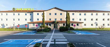 A B&B hotel with a central entrance, parking spaces, and a clear sky.