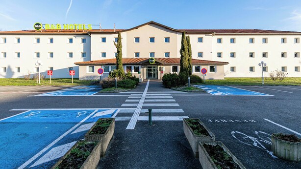 A B&B hotel with a central entrance, parking spaces, and a clear sky.