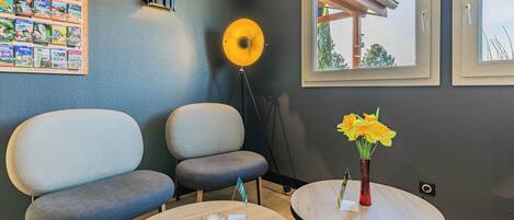 A modern waiting area with two grey chairs, a small round table with a vase of yellow flowers, and a wall-mounted photo display.
