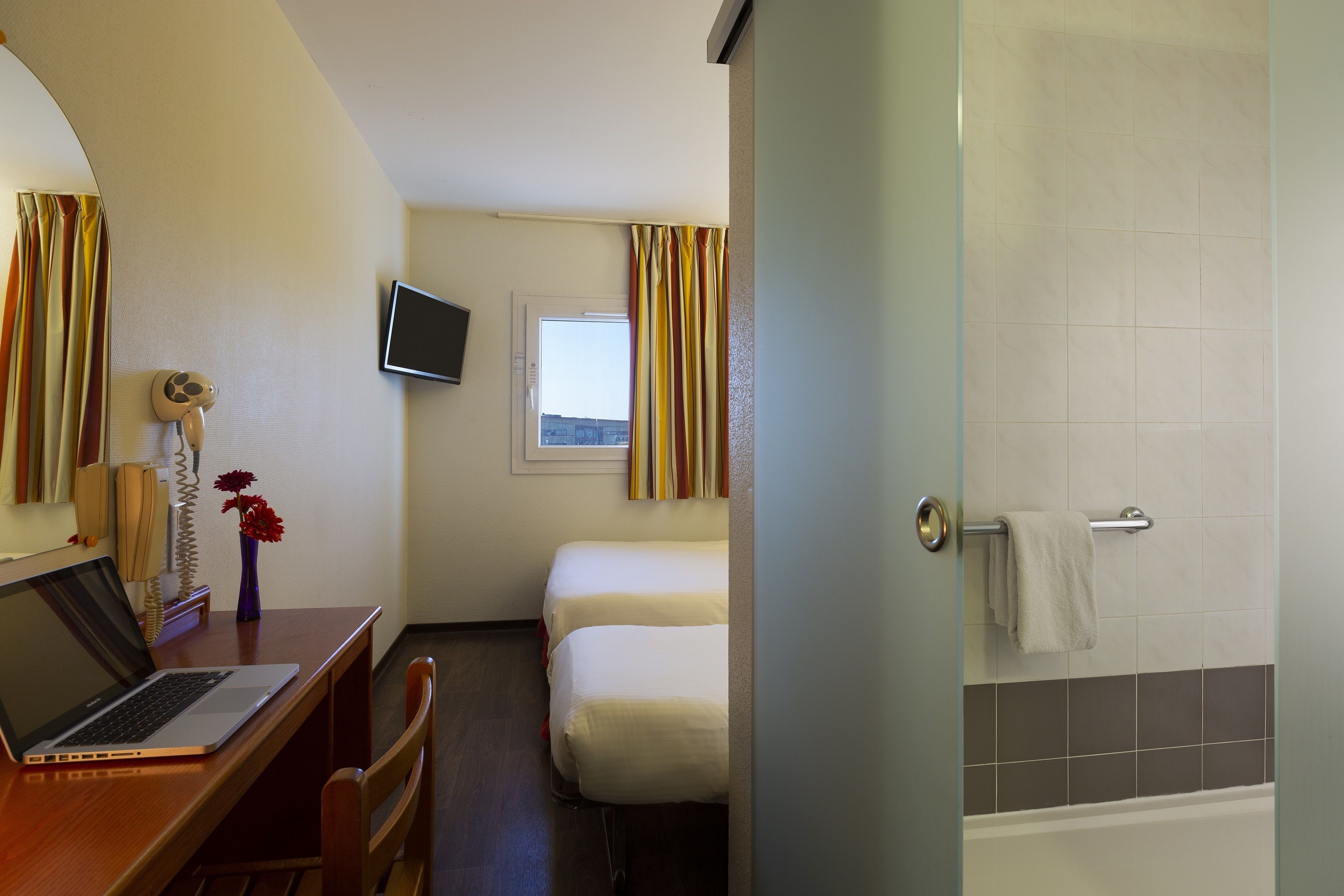 Habitación de hotel con escritorio, laptop, dos camas, televisor y ducha.