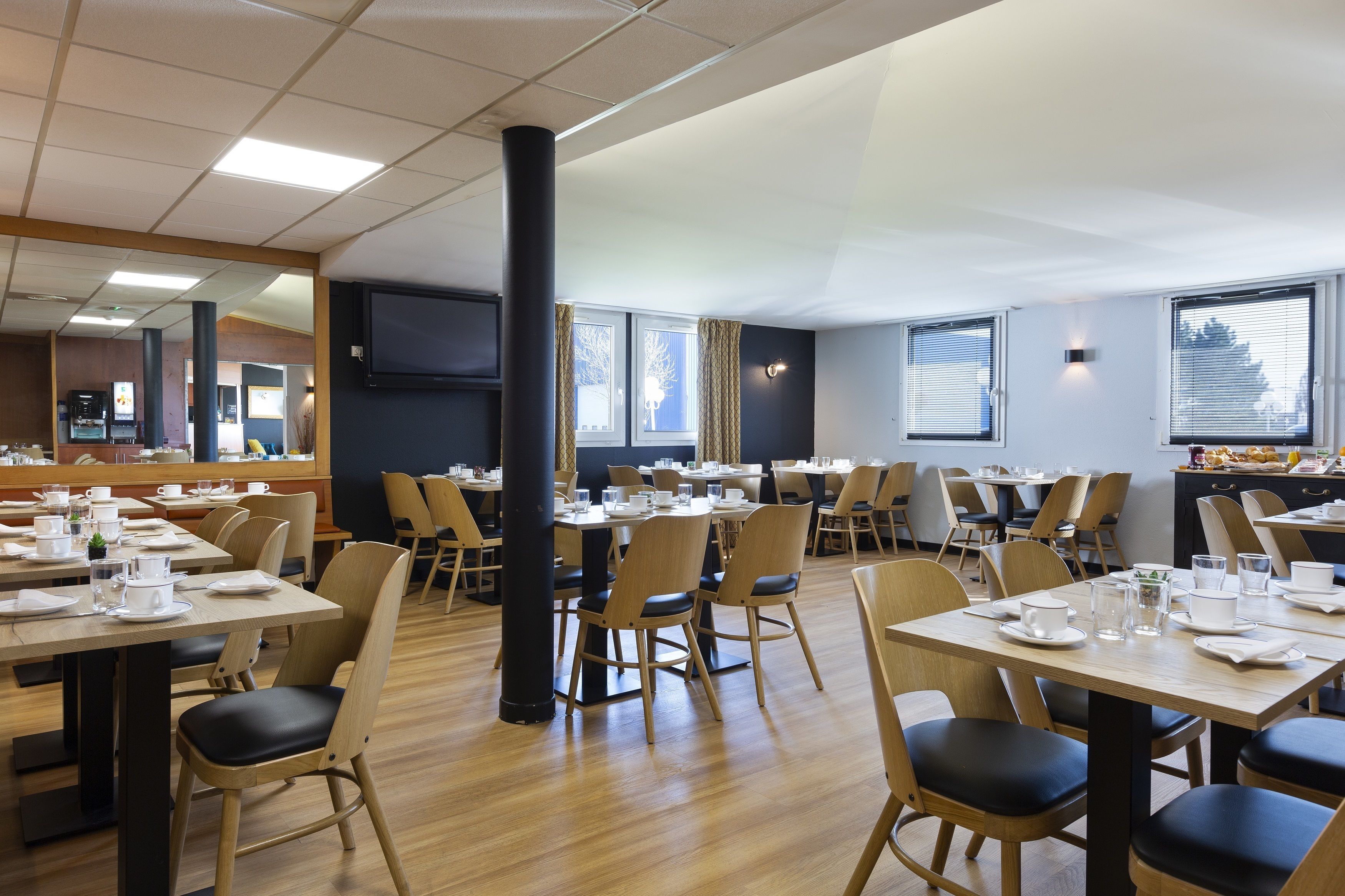 Un vaste espace dédié à la salle à manger, avec plusieurs tables et chaises, de grandes fenêtres et un téléviseur à écran plat fixé au mur.