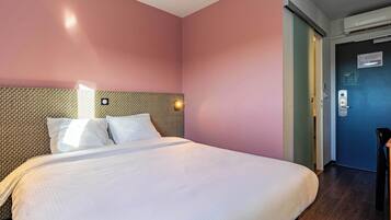 Ein Hotelzimmer mit einem großen Bett, einer strukturierten Kopfteil und einer Tür mit Schloss und Lichtschalter.