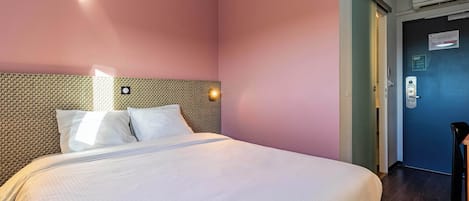 A hotel room with a large bed, a textured headboard, and a door with a lock and a light switch.