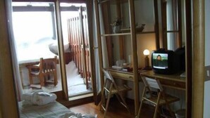 Una habitación con cama, escritorio, silla, televisor y ventana.