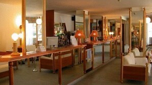 Un vestíbulo de hotel con un mostrador de recepción alargado, varios espejos y zonas de estar.