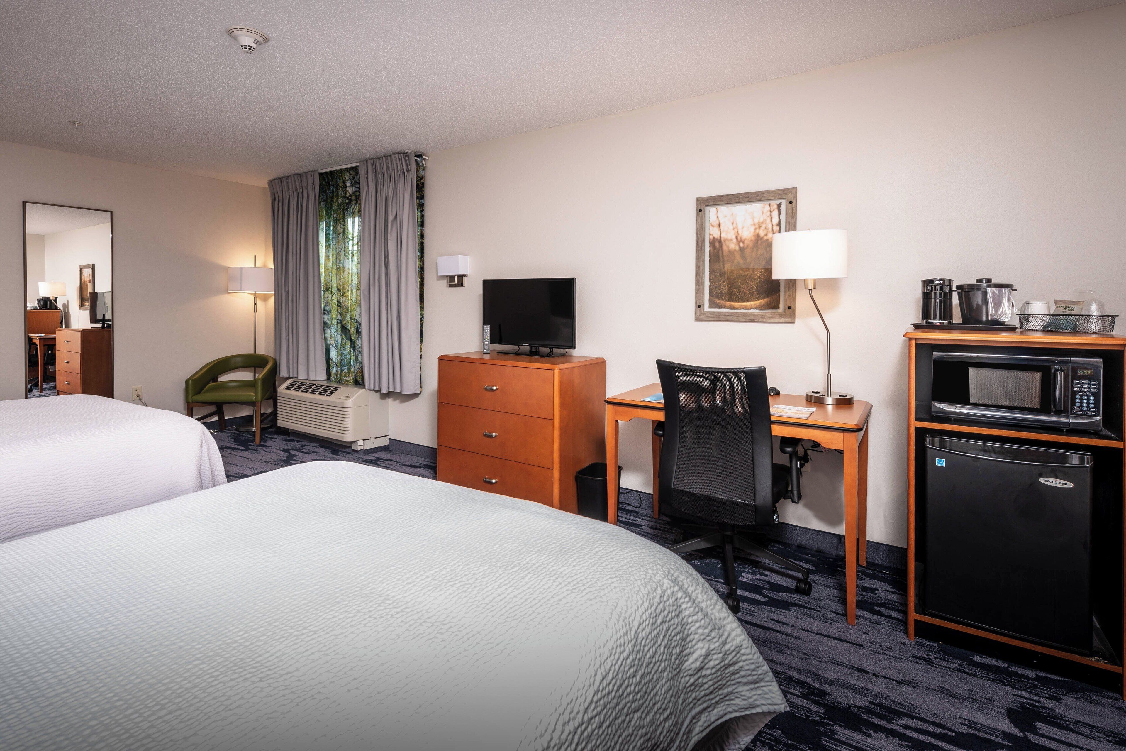 Habitación de hotel con dos camas, un escritorio con computadora, televisor, microondas y refrigerador.