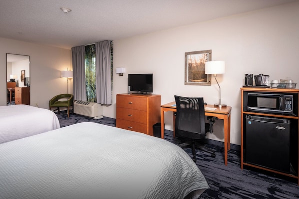 A hotel room with two beds, a desk with a computer, a television, a microwave, and a refrigerator.
