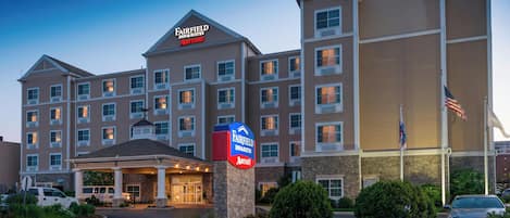A Fairfield Inn & Suites by Marriott hotel with a central entrance, multiple floors, and a flagpole with an American flag.