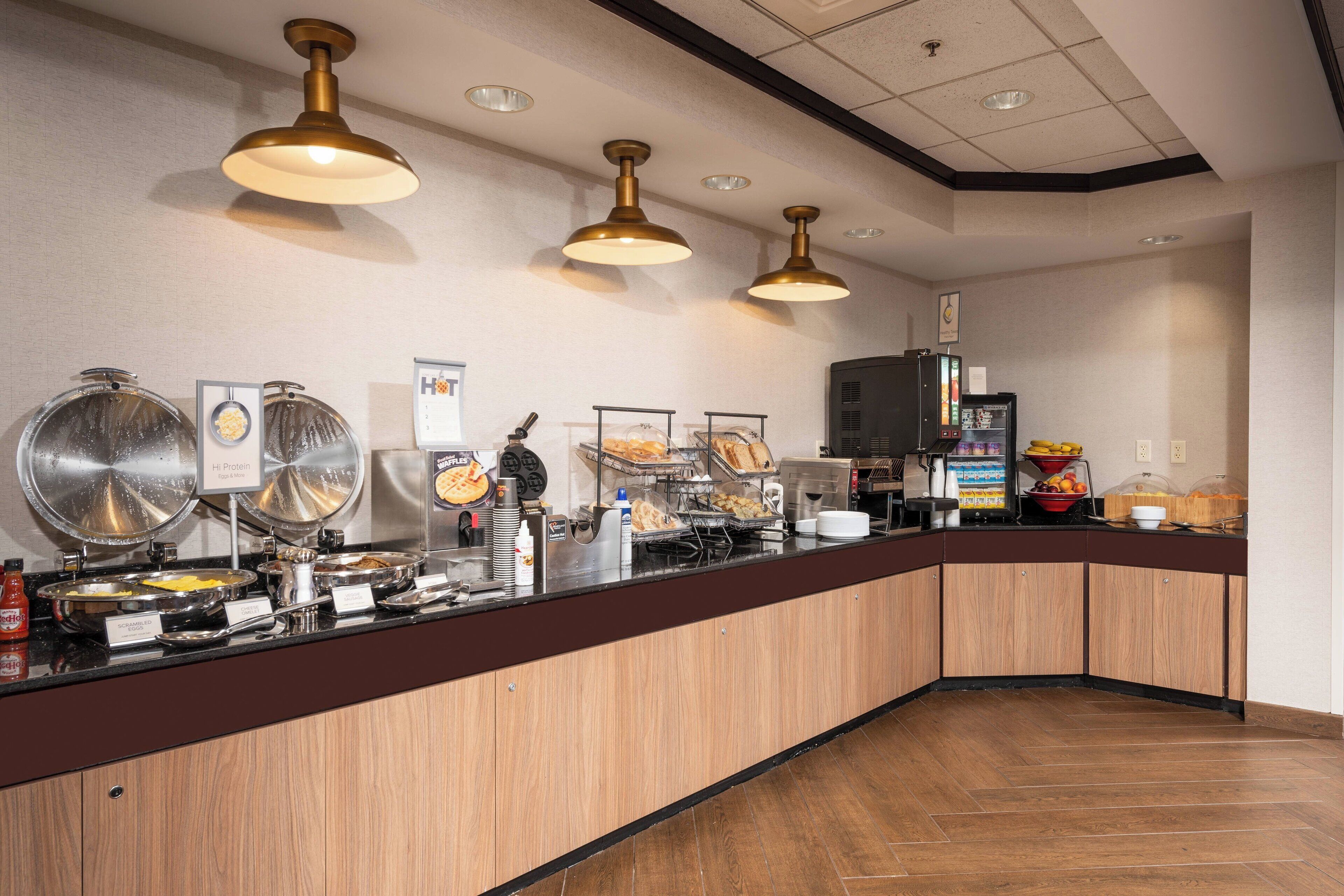 A buffet area with various food stations, including a hot food station, a cold food station, and a beverage station. There are also several condiment dispensers and a coffee machine.