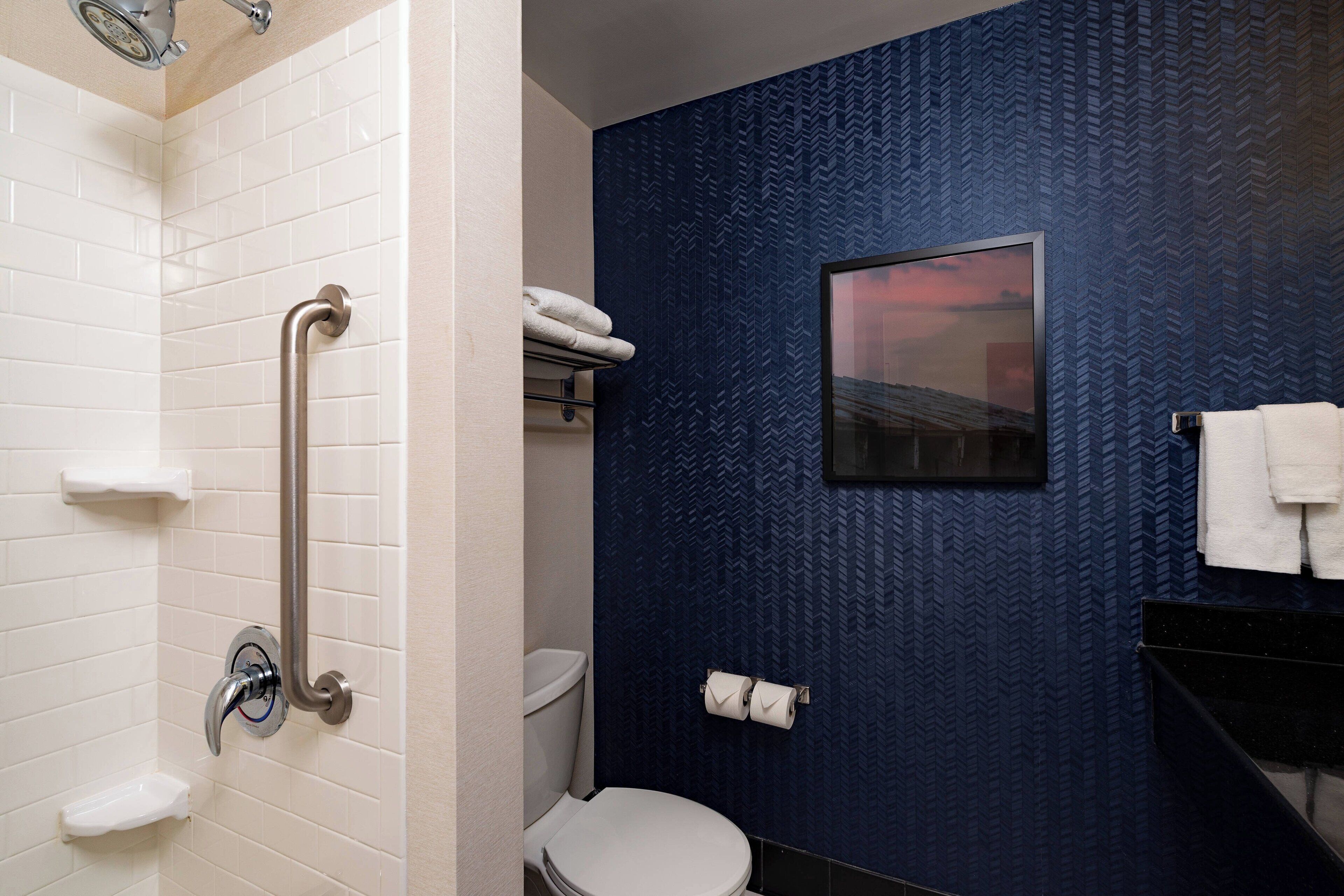 A bathroom with a white toilet, a blue textured wall, a sink with a towel rack, and a shower with a grab bar.