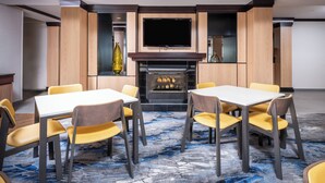 Une chambre d’hôtel dotée d’une cheminée, d’un téléviseur à écran plat et d’un coin repas avec des chaises jaunes et une table blanche.