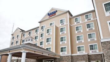 Un hotel de varios pisos con fachada color beige, una señal clara de Fairfield Inn & Suites by Marriott, y una entrada cubierta con columnas.
