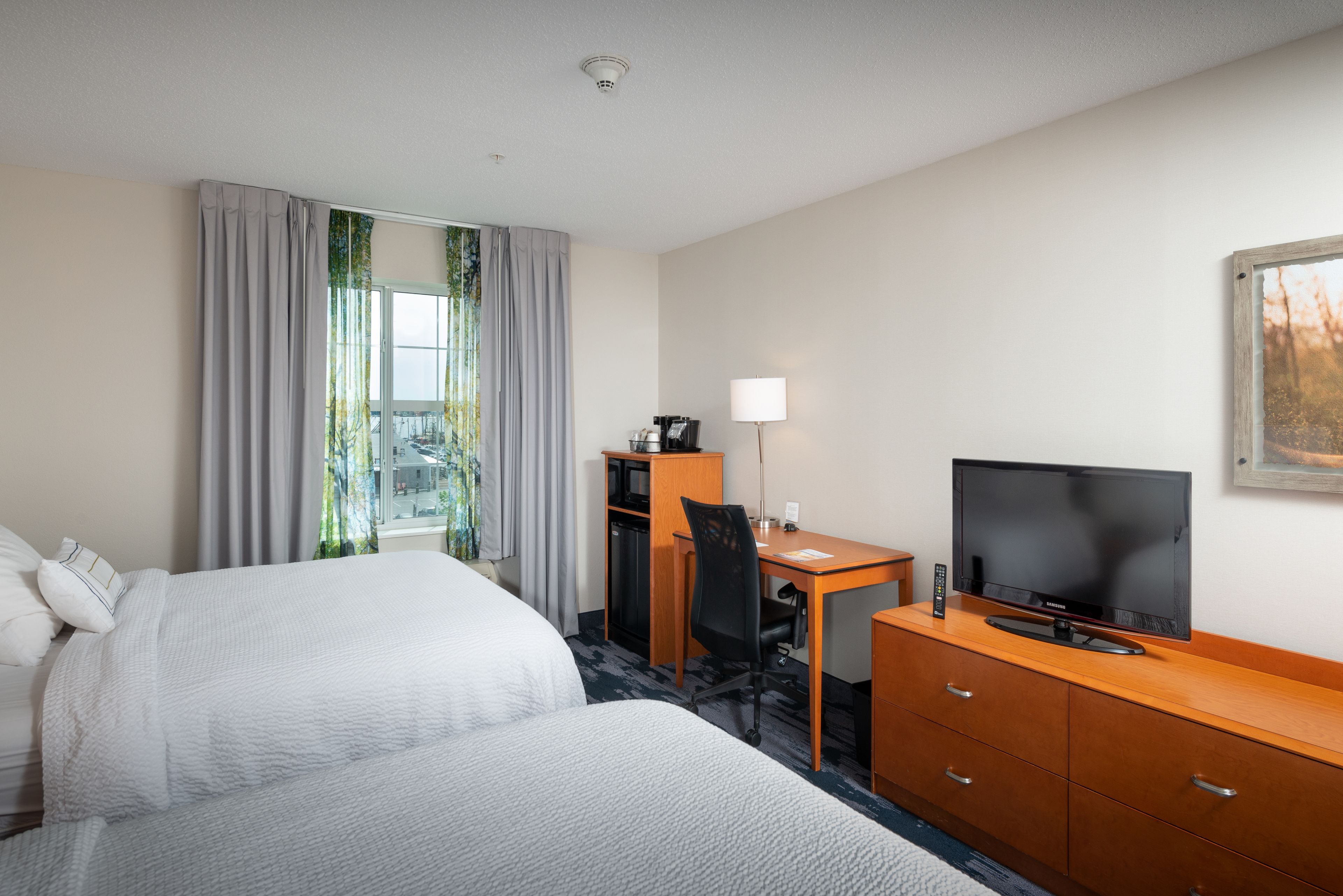 Habitación de hotel con dos camas, un escritorio, un televisor y una ventana con cortinas.
