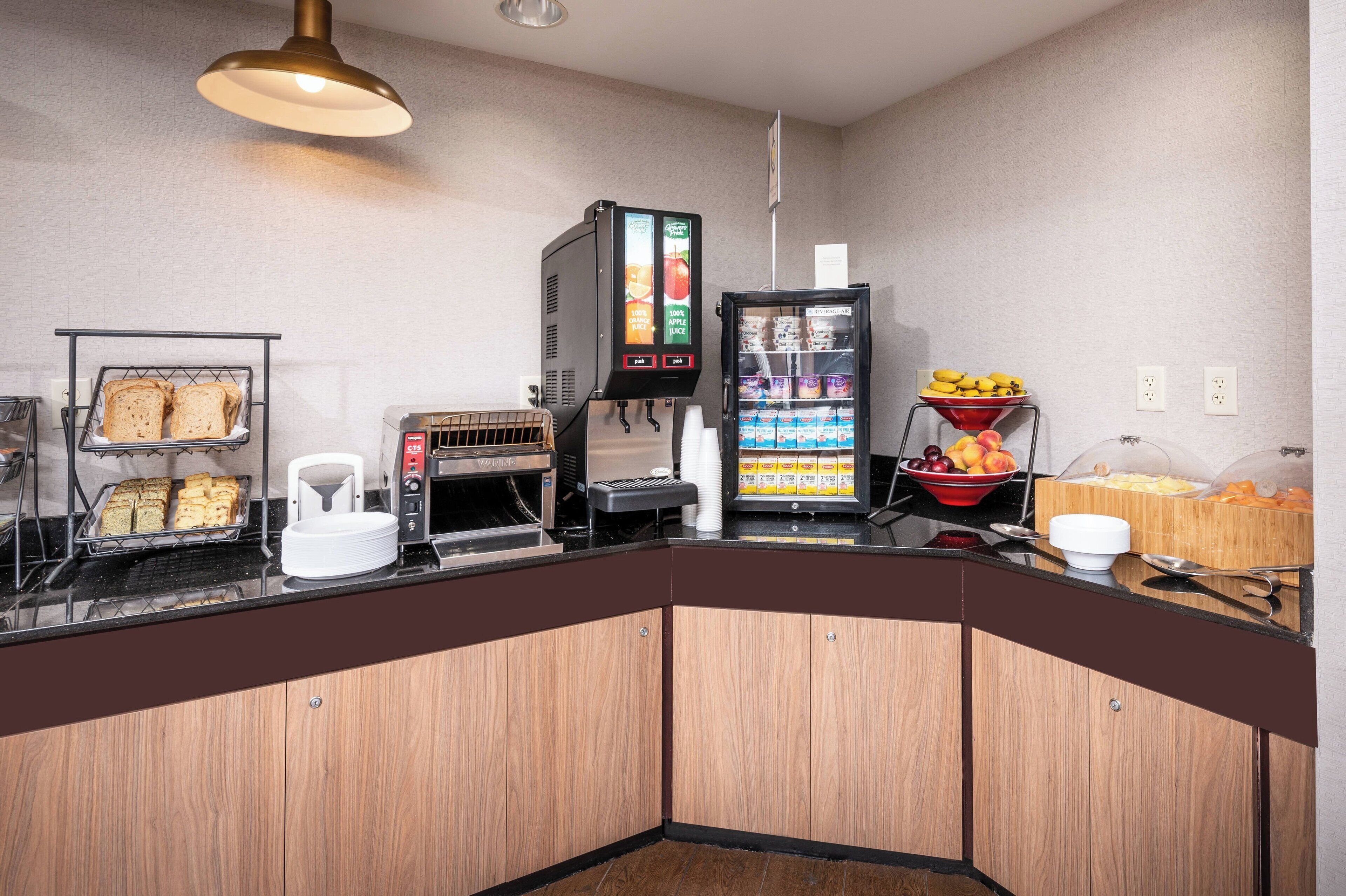 Un bar pour le petit-déjeuner équipé d’une machine à café, d’un réfrigérateur rempli de boissons et d’un panier de fruits.