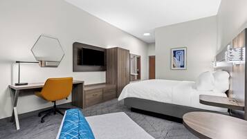 A modern hotel room with a bed, a desk, an office chair, a TV, and a bedside table.
