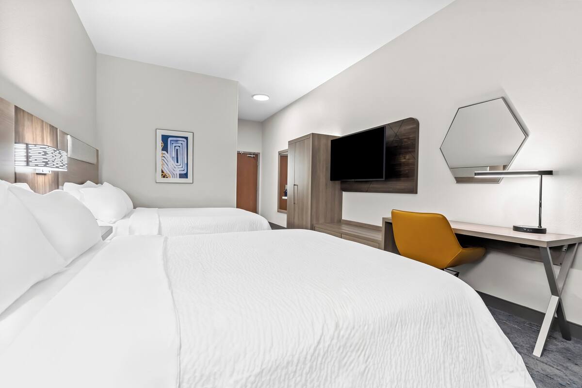A hotel room with two beds, a desk, a chair, a flat-screen TV, and a large mirror.
