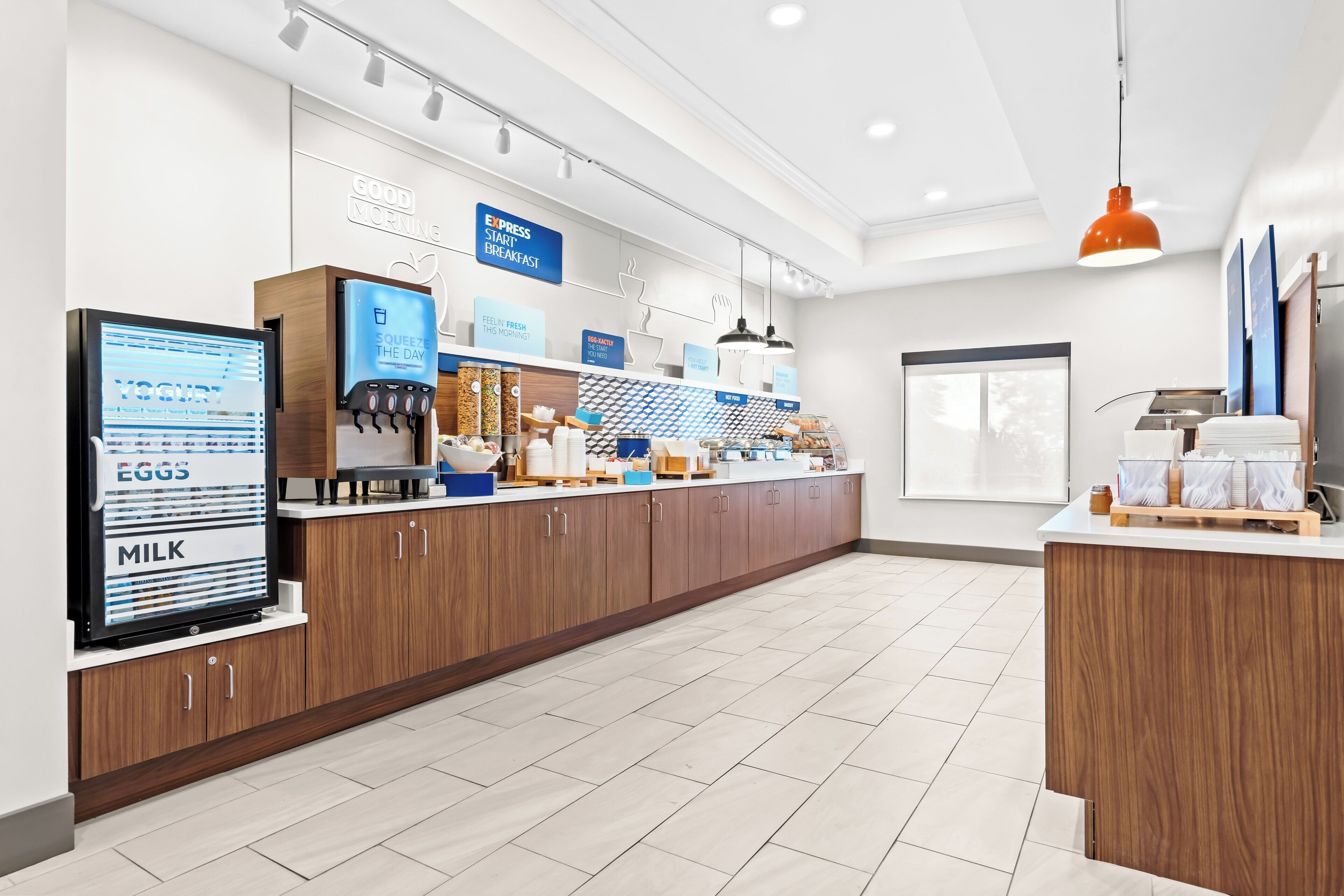 A modern breakfast area with a digital menu display, wooden cabinets, and a clean, tiled floor.