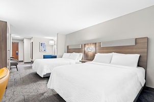 A hotel room with two beds, a desk, a chair, and a large window.