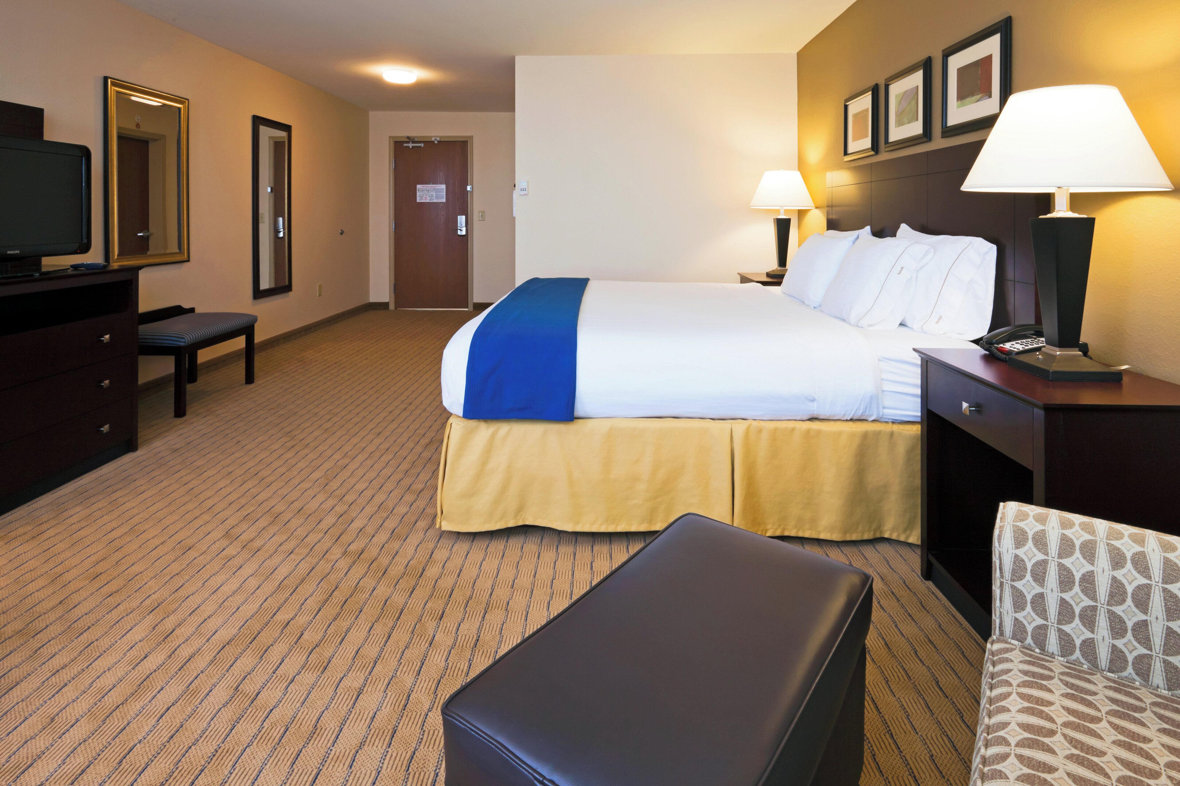 A hotel room with a bed, a desk, a chair, a television, and a lamp.
