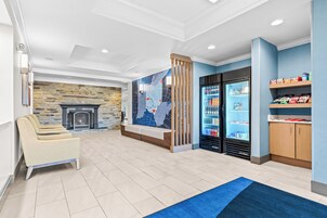 A modern lobby with a stone fireplace, a seating area, a refrigerator stocked with beverages, and a map mural on the wall.