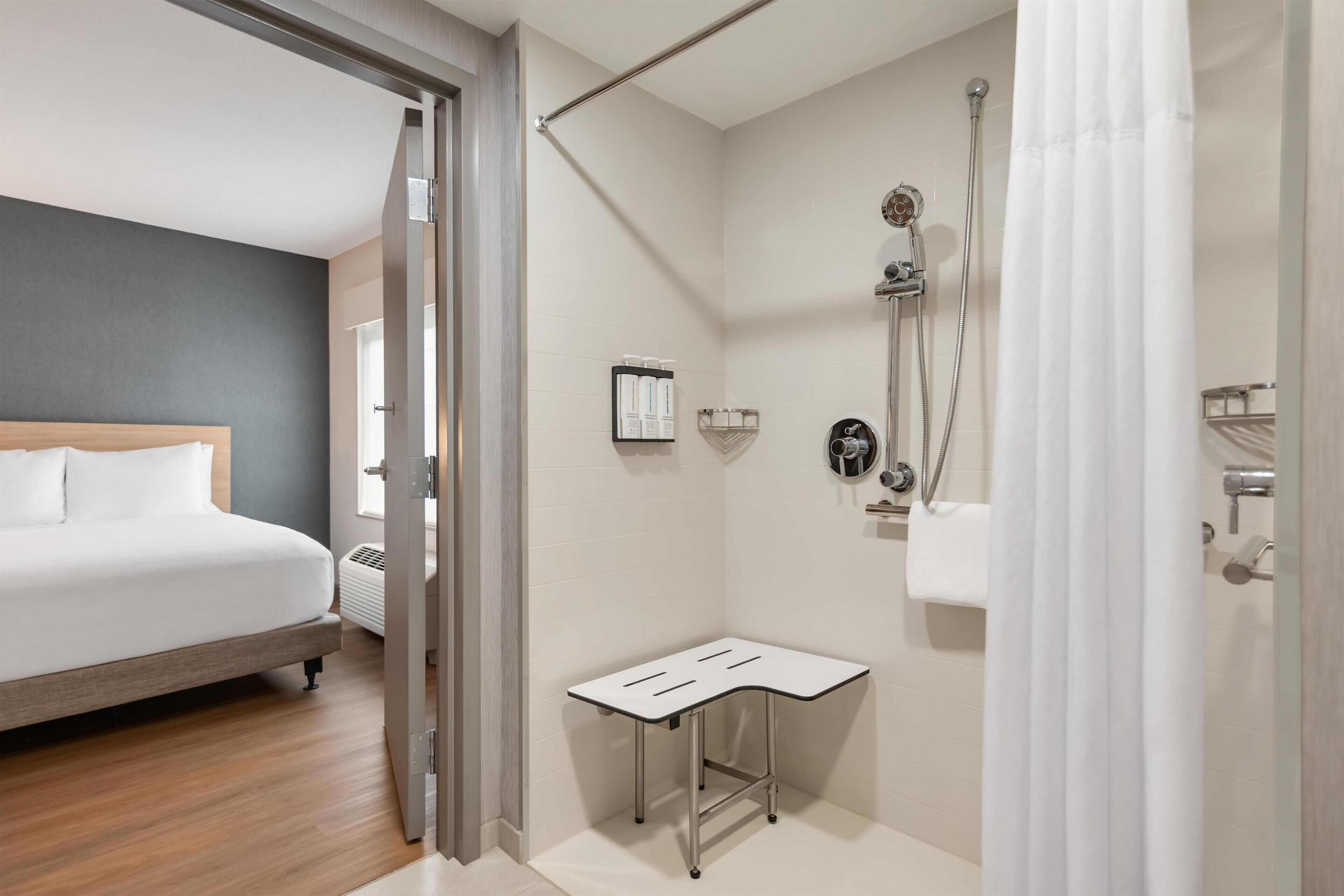 A modern hotel room with a bed, a shower area, and a small table.