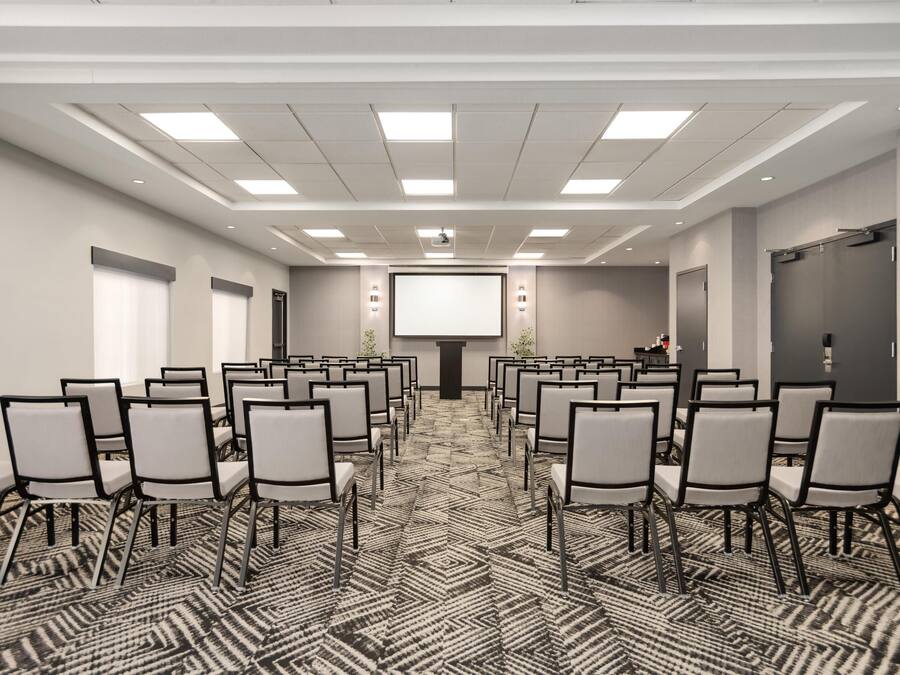 Une salle de conférence avec des rangées de chaises, un écran de projection et un pupitre.