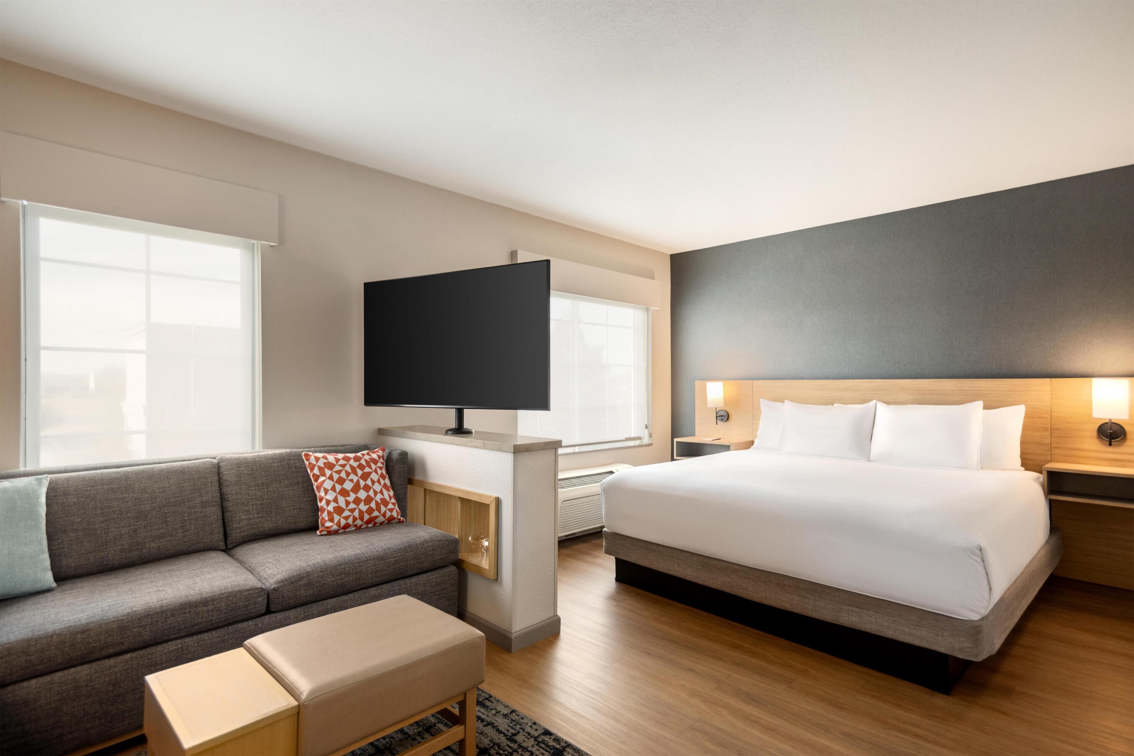 A modern hotel room with a sofa, a bed, a flat-screen TV, and a bedside table.