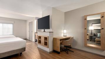 Una habitación de hotel con cama, escritorio, silla, televisor y espejo.
