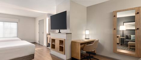 Una habitación de hotel con cama, escritorio, silla, televisor y espejo.