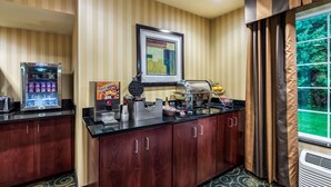 A hotel room with a kitchenette, including a coffee maker, waffle maker, and a framed artwork on the wall.