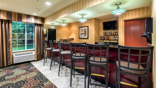 A bar area with a long counter, multiple bar stools, and a television mounted on the wall.