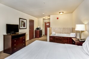 A hotel room with a bed, a dresser, a television, a desk with a lamp, and a bathroom with a bathtub and towel rack.
