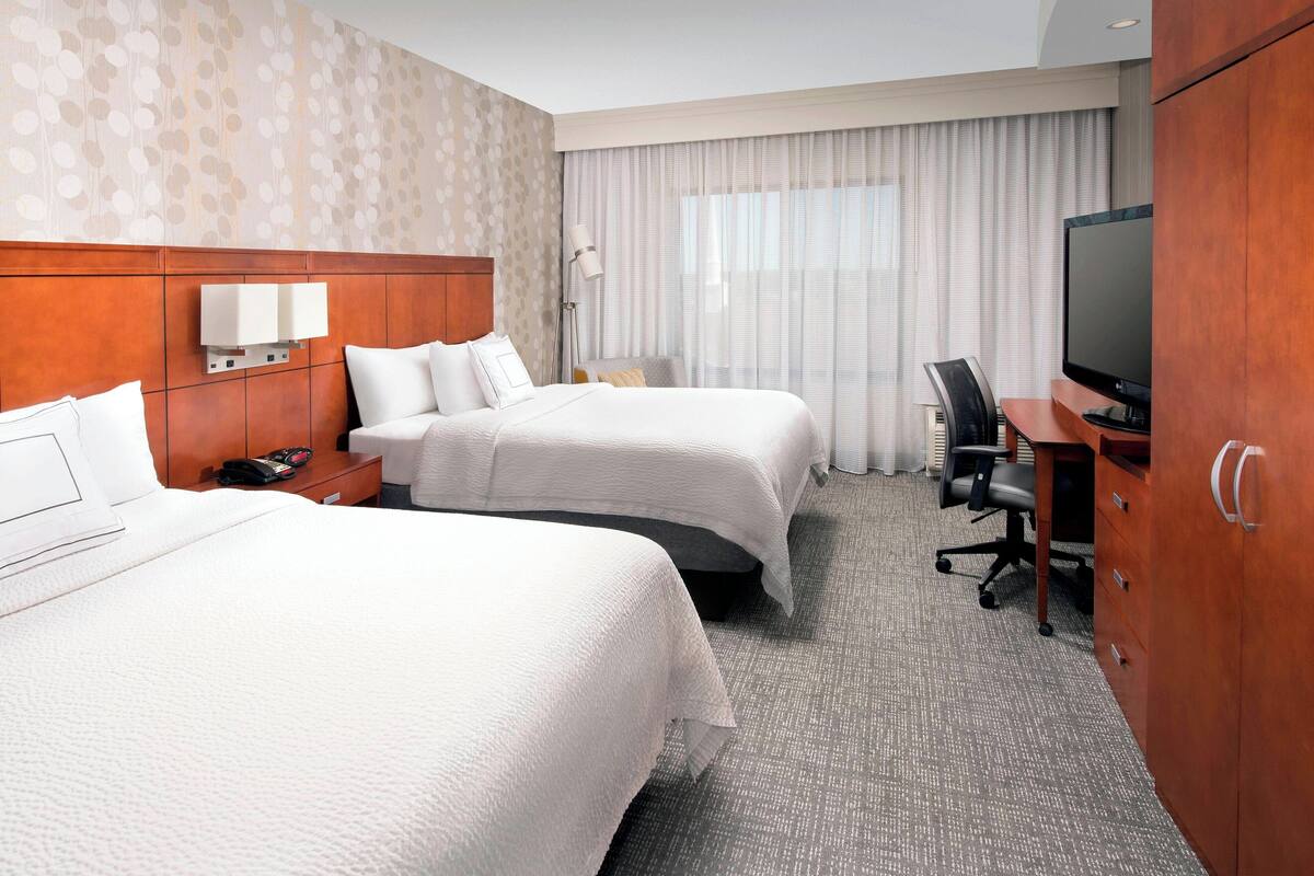 Habitación de hotel con dos camas, un escritorio con silla, televisor y armario.