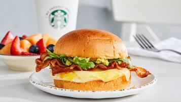 A breakfast sandwich on a plate with a Starbucks cup in the background.