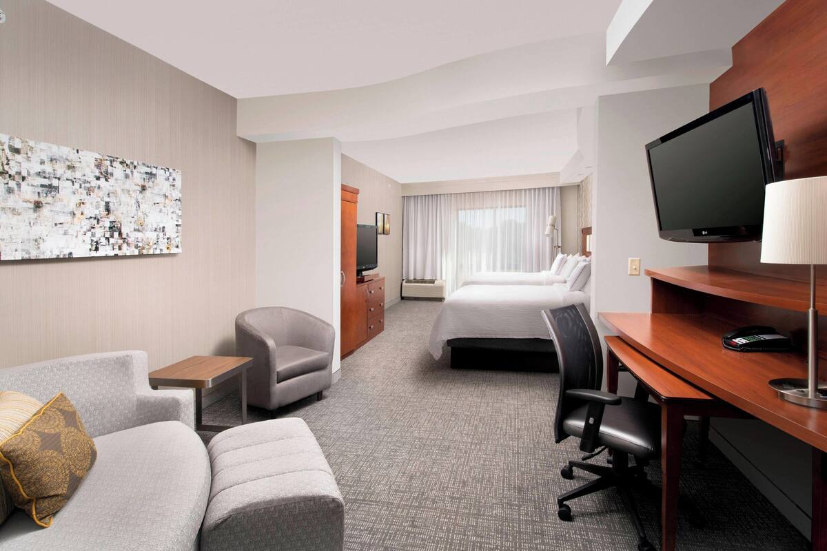 Una habitación de hotel con cama, escritorio, televisor, silla y sofá.