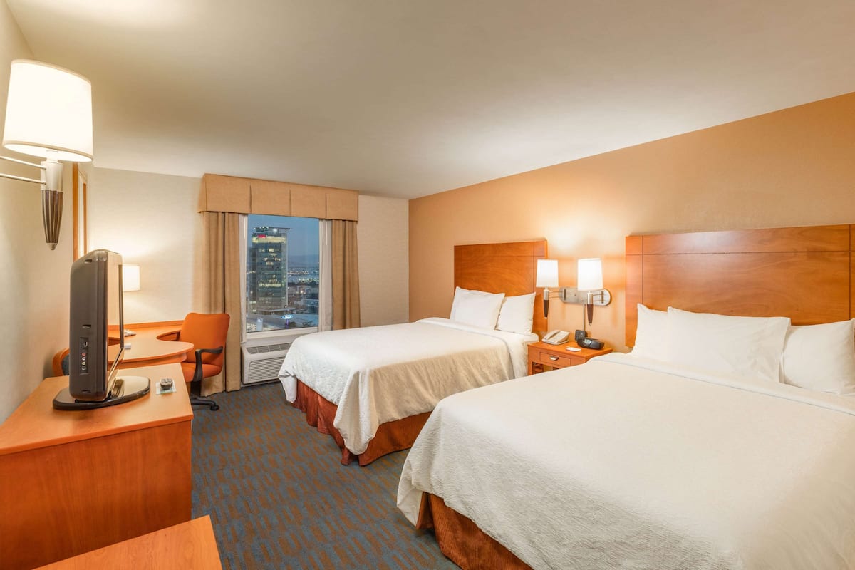 A hotel room with two beds, a desk with a computer, a chair, and a view of a cityscape.