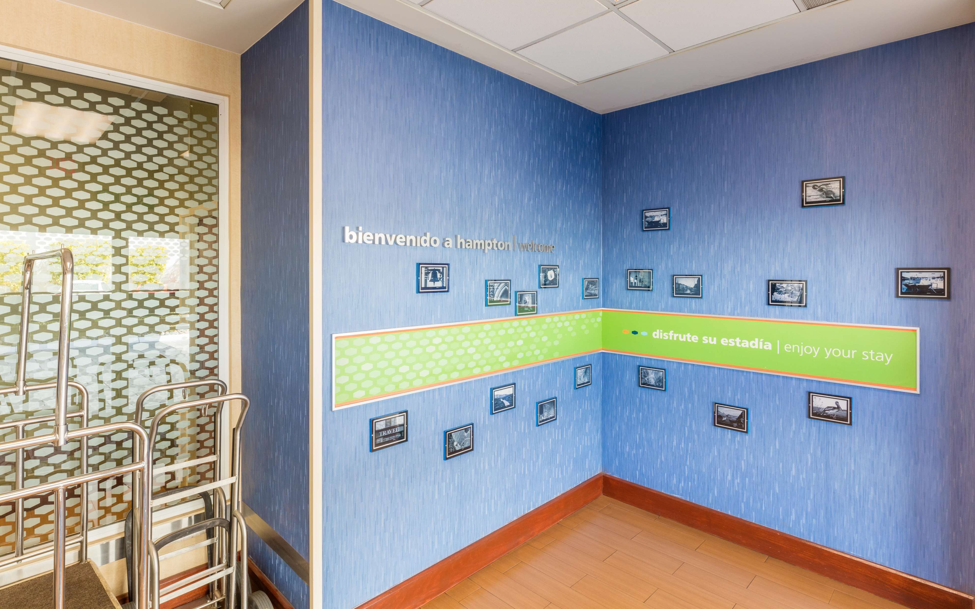 Een blauwe gang met een bord van harte welkom, een groene strook met een boodschap en meerdere afbeeldingen in lijsten aan de muur.