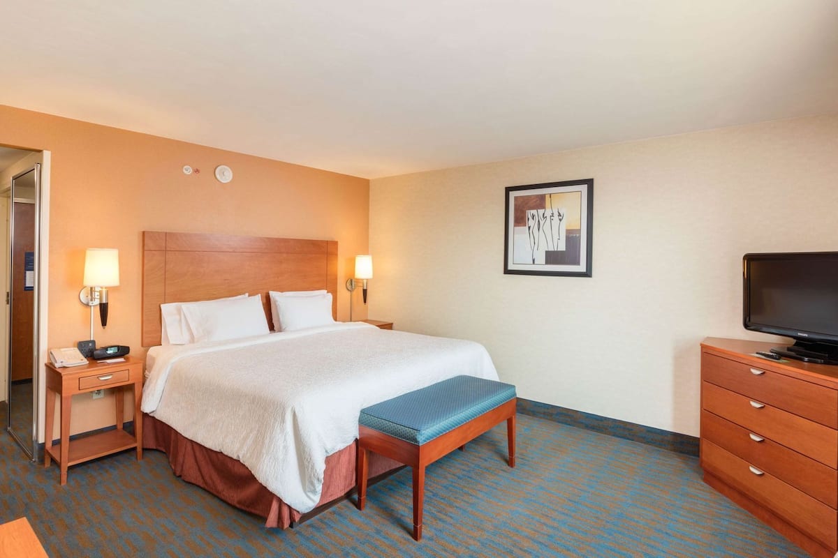 A hotel room with a bed, bedside lamps, a television, a desk, and a chair.