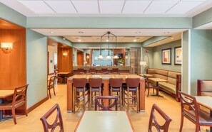 A hotel dining area with a central bar, multiple seating options including tables and booths, and a modern ceiling design. - Hampton Inn by Hilton Queretaro Tecnologico (Querétaro)