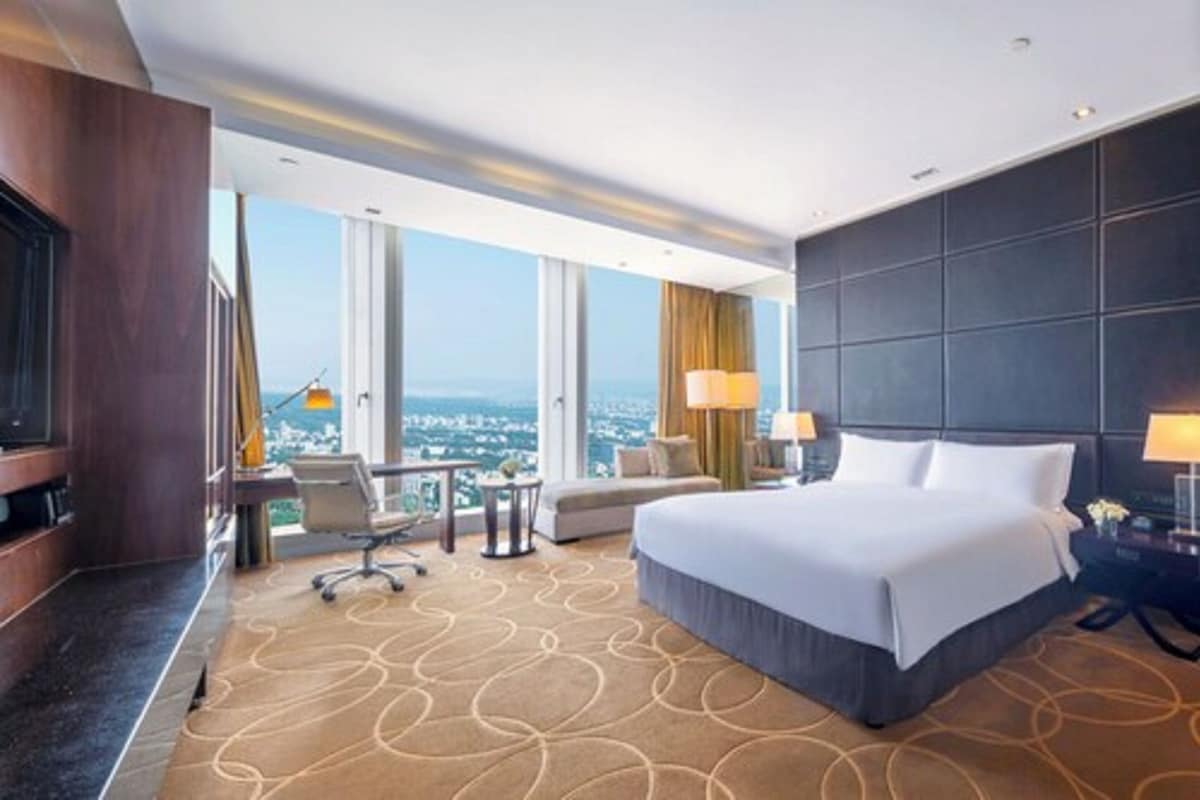 A hotel room with a large bed, a desk with a chair, a TV, and a view of the city.