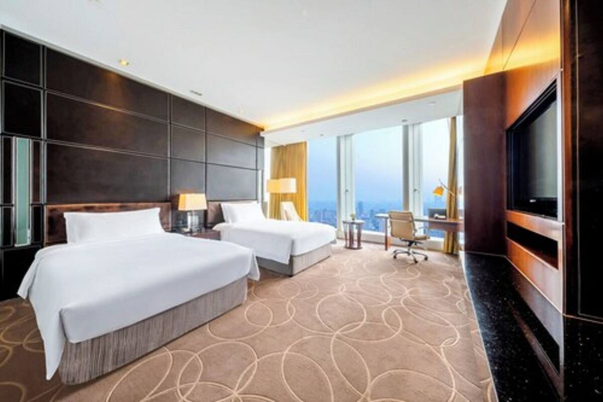 Quarto de hotel com duas camas, televisão, escrivaninha e vista para a cidade.
