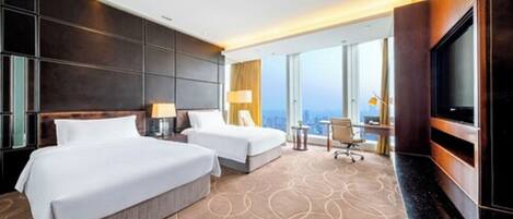 A hotel room with two beds, a TV, a desk, and a view of the city.