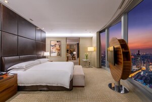 Una habitación de hotel moderna con una cama grande, un escritorio y vistas de la ciudad al atardecer.