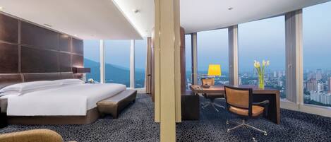 Habitación de hotel con una cama grande, un escritorio con silla, vistas a la ciudad y un ventanal amplio.