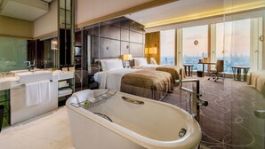 Une chambre d’hôtel moderne dotée d’une grande baignoire, d’une salle de bain séparée, d’une vue sur la ville et d’un bureau avec une chaise.