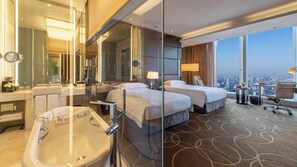 Habitación de hotel con una bañera grande, dos camas, un escritorio con silla y vistas a la ciudad.